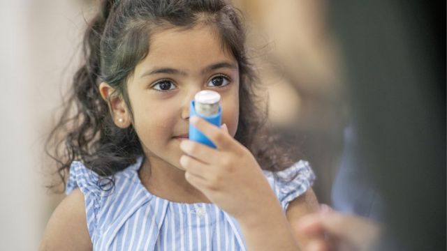 A child girl holding an asthma inhaler in front of her face