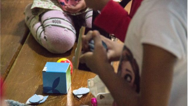 Foto mostra meninas brincando com itens de papelaria, seus rostos não são visíveis