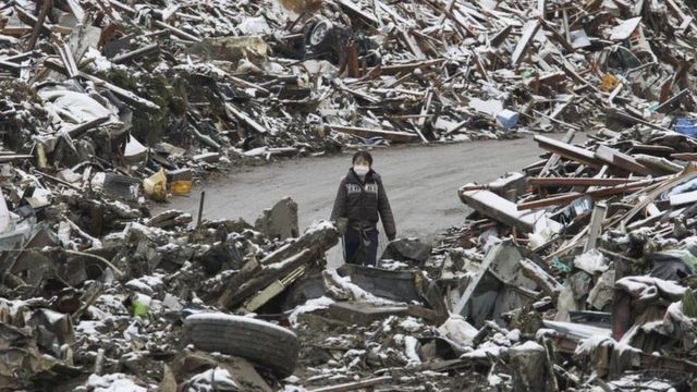 Uma mulher caminha entre os escombros na cidade japonesa de Minamisanriku, no norte do Japão, após o tsunami de 2011.