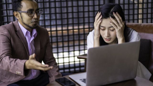 Mujer estresada hablando con un compañero frente a una computadora.