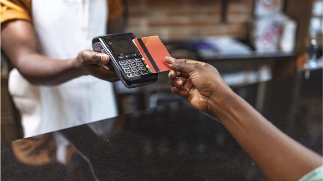 Mão segurando cartão próximo à maquina de pagamento