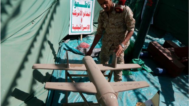 جندي حوثي يتفقد نماذج صواريخ وطائرات بدون طيار.