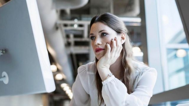 Una mujer contemplando, con expresión de aburrimiento, la pantalla de la computadora