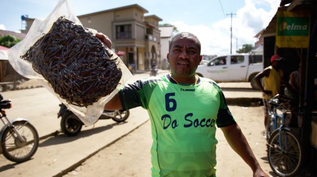 Imagem mostra homem segurando pacote transparente cheio de favas de baunilha em uma rua de Madagascar. Ele é um 'atravessador', ou seja, compra o produto dos agricultores para revender mais caro