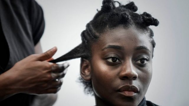 A woman has her hair plaited in a salon specialising in afro textured hair