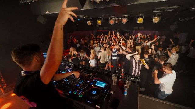DJ frente a jóvenes bailando en un club nocturno en Londres.