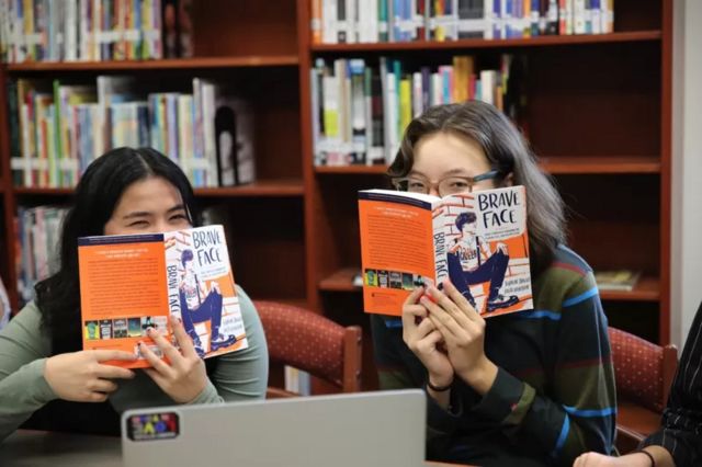 Jovens segurando livros em seus rostos.