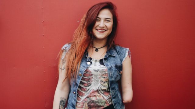 Mariana Torquato sorrindo em frente a parede vermelha