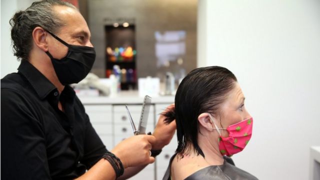 Cabelereiro corta cabelo de cliente na Alemanha, ambos usam máscaras
