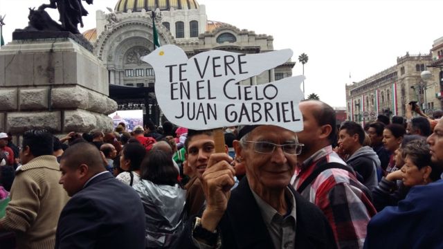 Hombre sostiene un cartel que dice "te veré en el cielo Juan Gabriel".