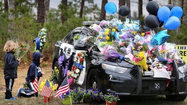 Дети возлагают цветы к автомашине массачусетского полицейского Шона Гэннона, застреленного в апреле 2018 года, когда он пытался вручить ордер на арест