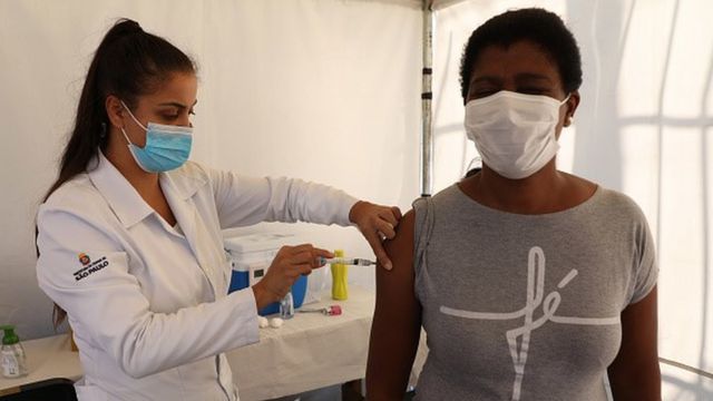 Enfermeira aplica vacina em braço de mulher