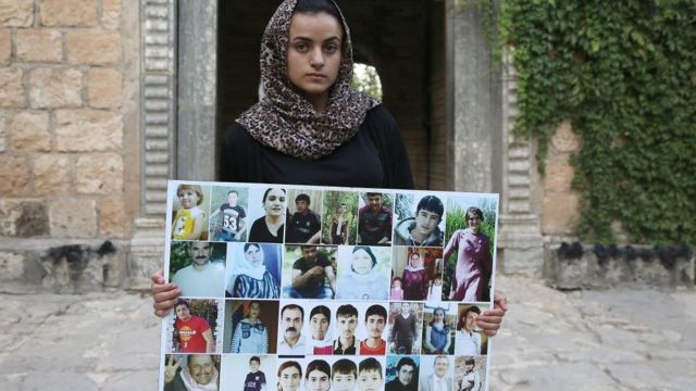 احدى الناجيان من السبي تحمل صور المفقودين من أهلها