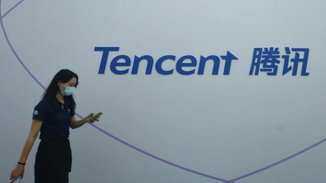 Uma mulher andando em frente a um logo da Tencent