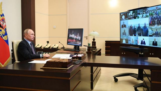 Russian President Vladimir Putin faces a TV screen with a number of officials on a video conference