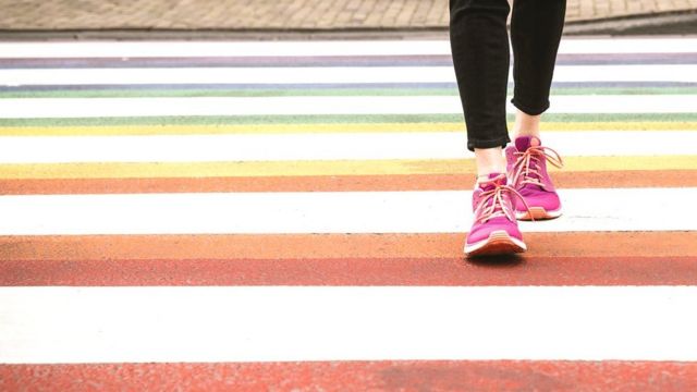 Foto mostra detalhe de pés atravessando a rua