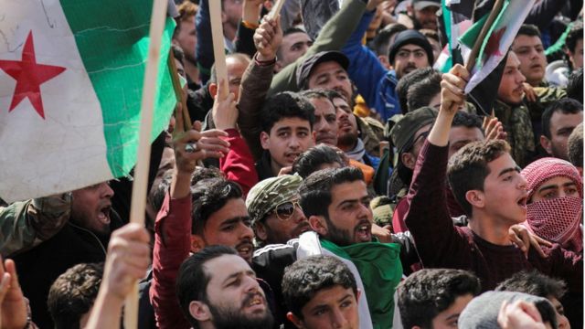 أشخاص يحملون لافتات وأعلام المعارضة خلال مظاهرة بمناسبة الذكرى العاشرة لبدء الصراع السوري في إدلب التي تسيطر عليها المعارضة