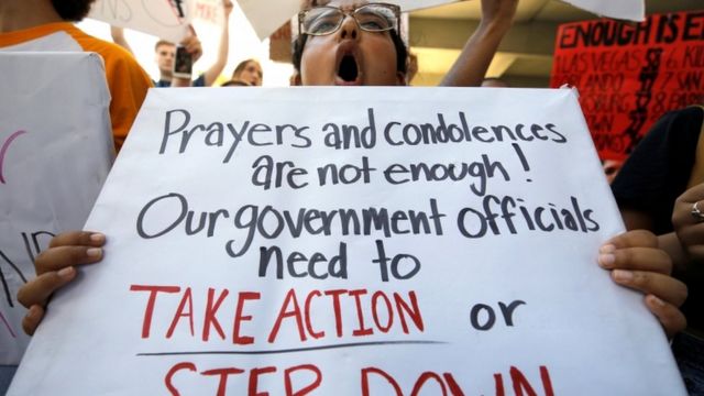 A student holds a sign saying "prayers and condolences aren't enough! Our government officials need to take action or step down"