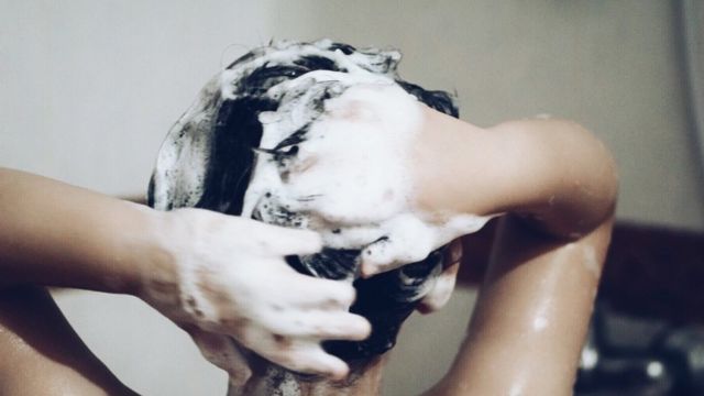Una persona lavándose el cabello con shampoo