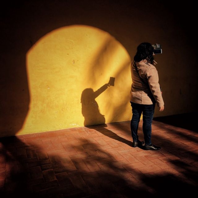 A woman takes a picture of herself as the sun shines through the archway she stands under