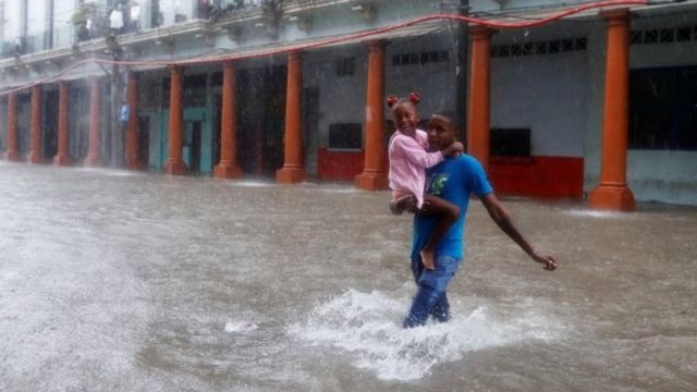 Un hombre carga a una menor en una calle inundada de La Habana