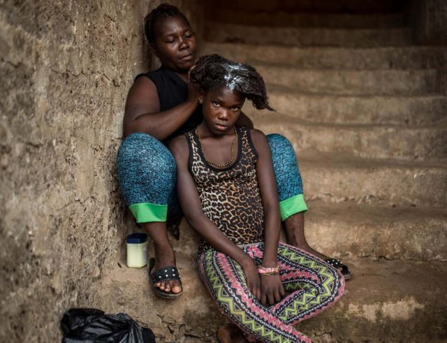 A mother washes her daughter's hair on the steps of the house