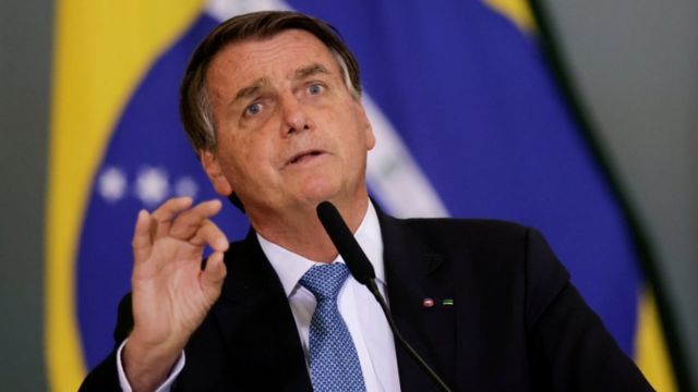 Bolsonaro discursa no microfone, com bandeira do Brasil atrás