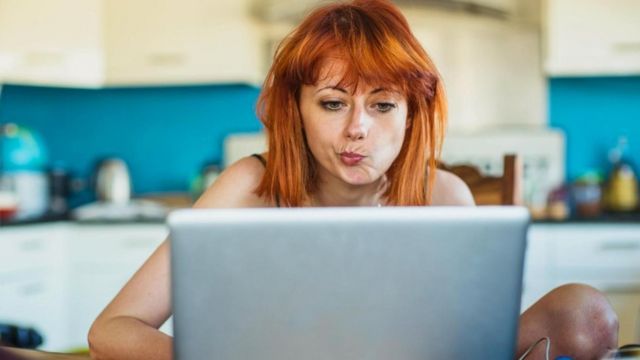 Una joven sentada frente a su laptop con rostro dudoso