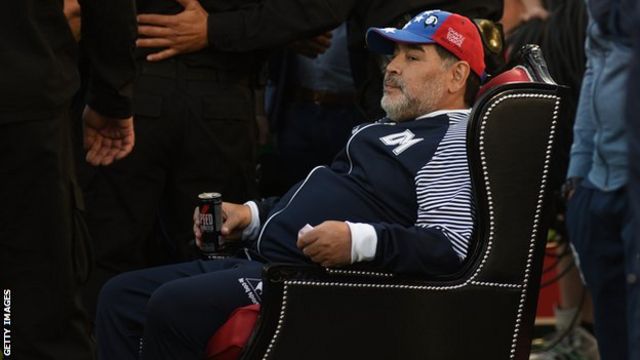 Maradona sits on a throne that is offered to him