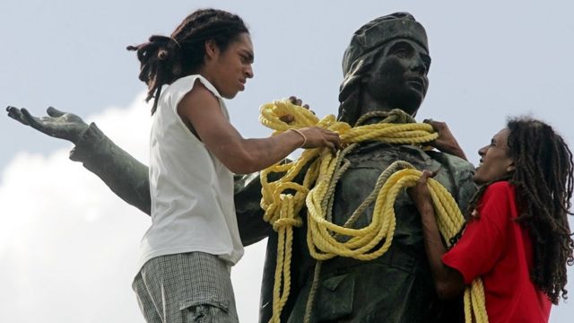 Dos jóvenes ponen una cuerda sobre el cuello de la estatua