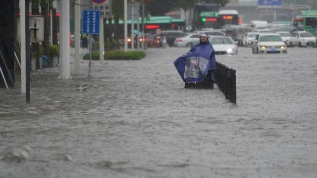 A resident wearing a rain cover stands on a flooded street in Zhengzhou