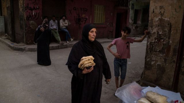 An Egyptian woman carries flat breads in a street in Cairo