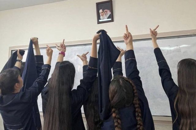 Estudiantes levantando el dedo medio, haciendo una seña que es considerada obscena, ante los retratos del ayatolá Jamenei y del fundador de la República Islámica, el ayatolá Ruholá Jomeini.