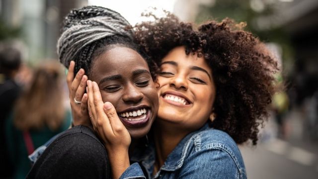 Two young women, best friends, smiling and hugging on the street.
