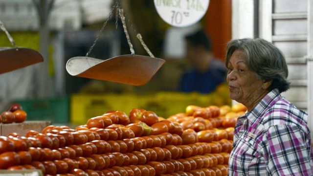 Una señora ante un puesto de tomates.