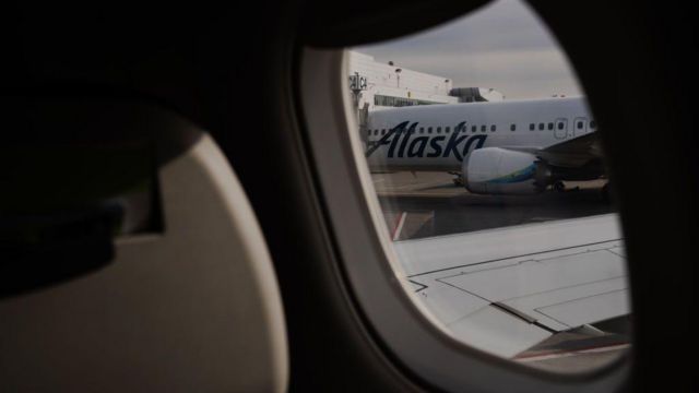 Imagen que muestra un avión de Alaska Airlines a través de la ventanilla de otro avión.