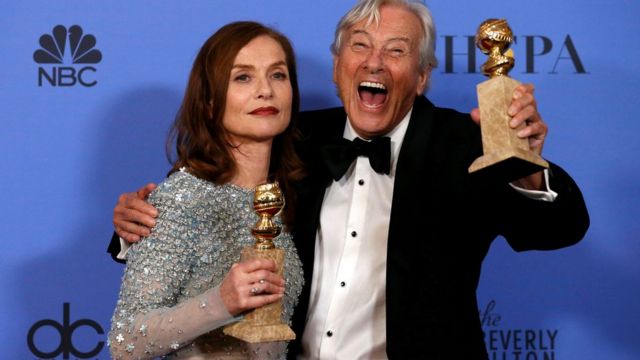 La actriz Isabelle Huppert y el director holandés Paul Verhoeven muestran dos premios globos de oro. El director sonríe y ella se muestra seria.