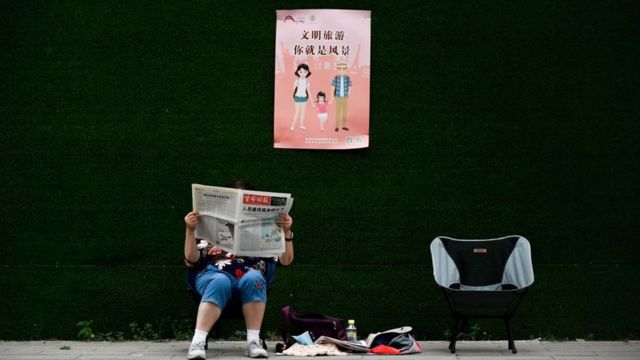 Mulher sentada em área pública lendo jornal