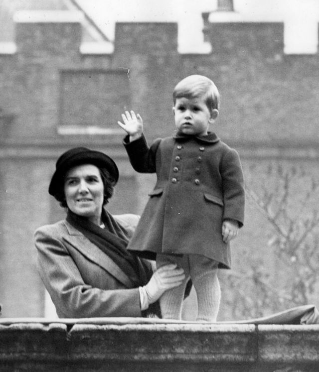 Charles waving to the crowd from the wall of Clarence House, London. Firmly held by nurse Lightbody, he is seen on the vantage point from which he watched his grandparents, the King and Queen, and his mother, Princess Elizabeth, driving to Westminster for a Parliament ceremony.