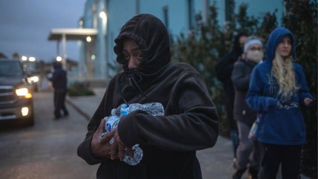 Mulher agasalhada segura garrafas de água retiradas em abrigo durante onda de frio no Texas