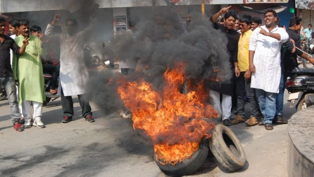 Hombres manifestándose con llantas quemadas en la calle.