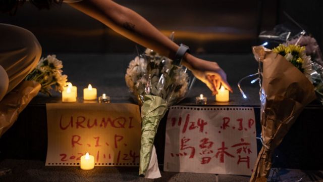 Lilin dan spanduk memperingati korban kebakaran Urumqi.