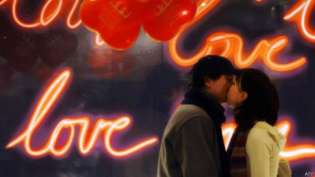 Namorados se beijam em frente a um letreiro luminoso