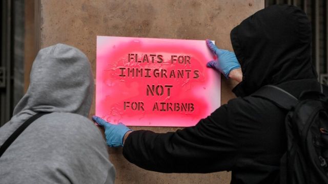 Activists stencil a slogan reading "Flats for immigrants not for airbnb" on a wall during a demonstration in Athens.