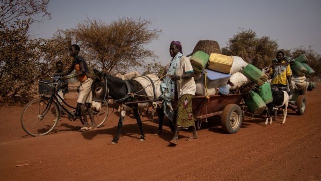 Des gens avec leurs affaires empilées sur une remorque de fortune tirée par un âne