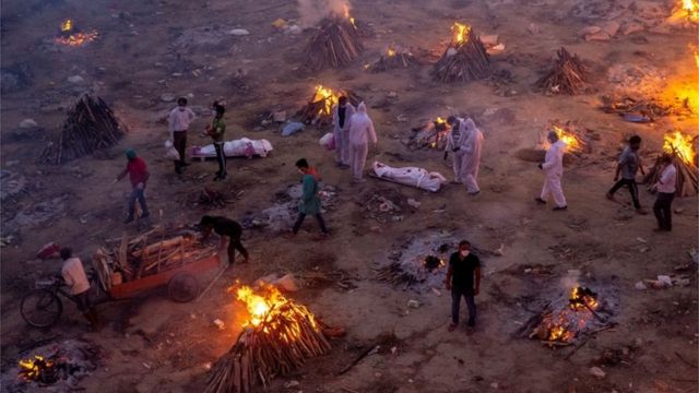 People walk past funeral pyres in New Delhi, India, April 2021