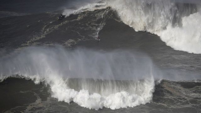 A surfer rides a wave in Nazaré, Portugal.
