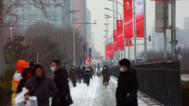 People bundled up in winter clothes walk down snow-covered streets in central Beijing