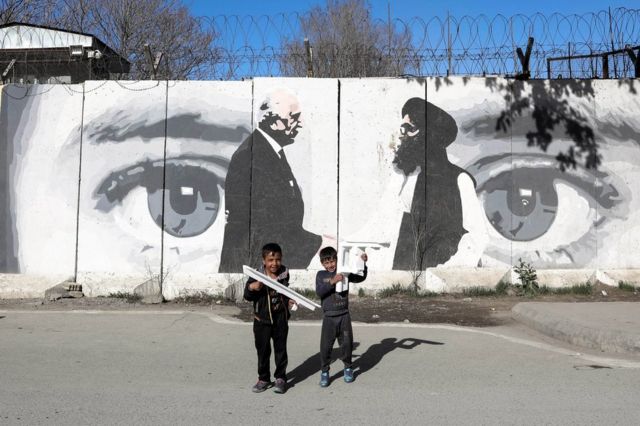 Afghan boys play in front of a wall painted with a photo of Zalmay Khalilzad, U.S. special envoy in Afghanistan (L), and Mullah Abdul Ghani Baradar, the leader of the Taliban delegation