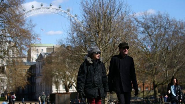 Pessoas caminham na rua em Londres com roda-gigante ao fundo